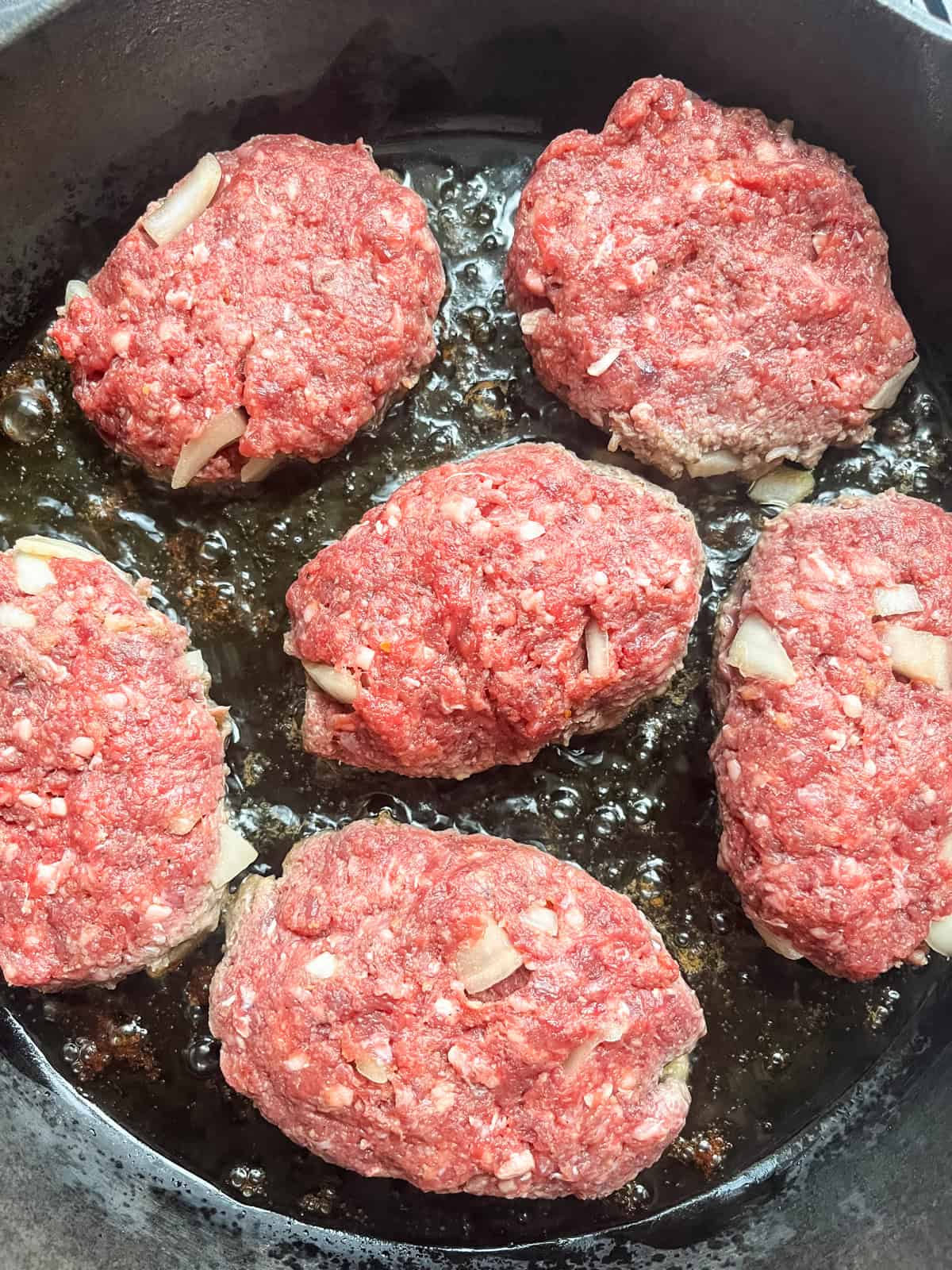 Salisbury steaks cooking in a cast iron skillet.