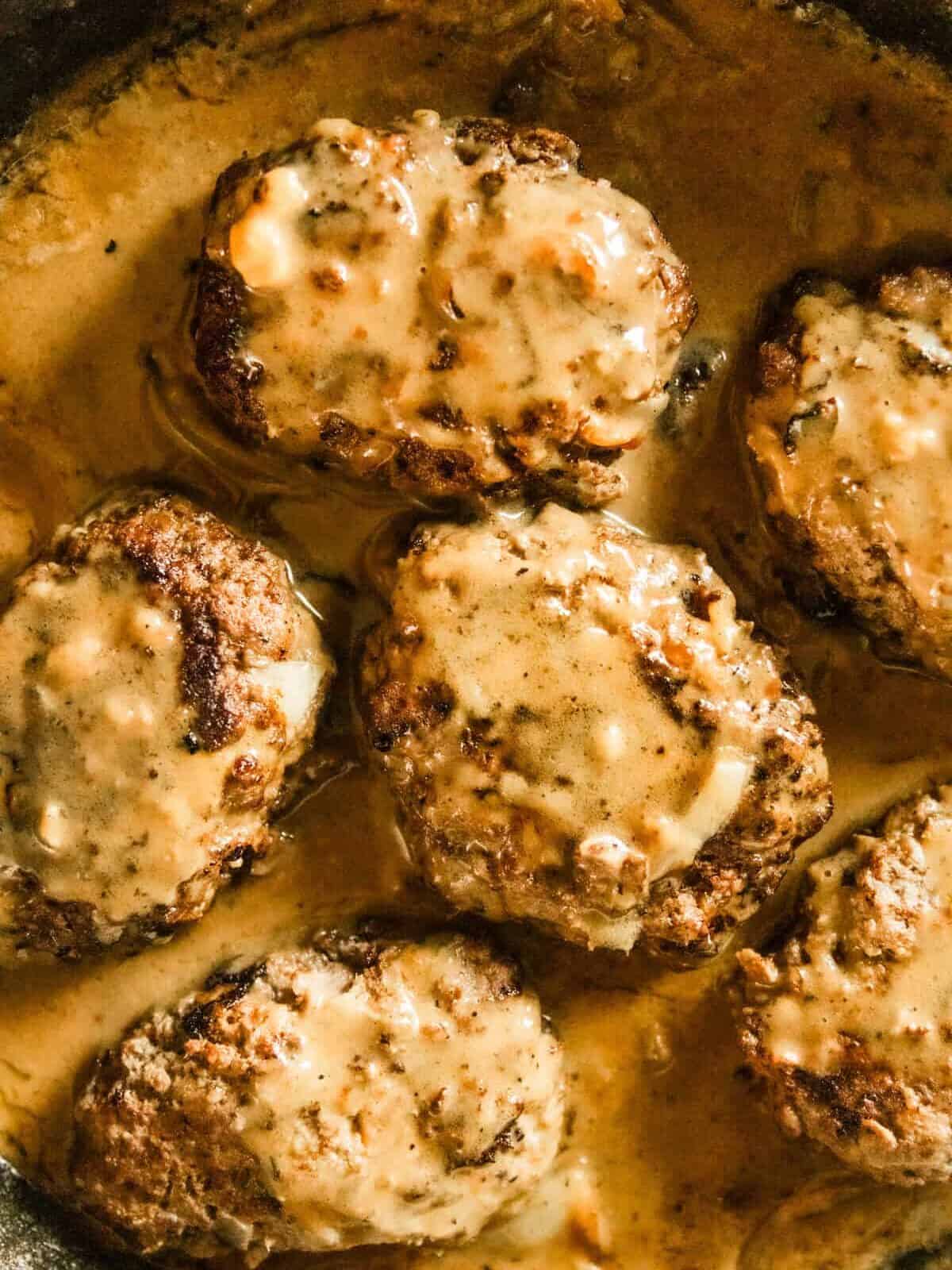 Venison salisbury steaks cooking in a cast iron skillet.