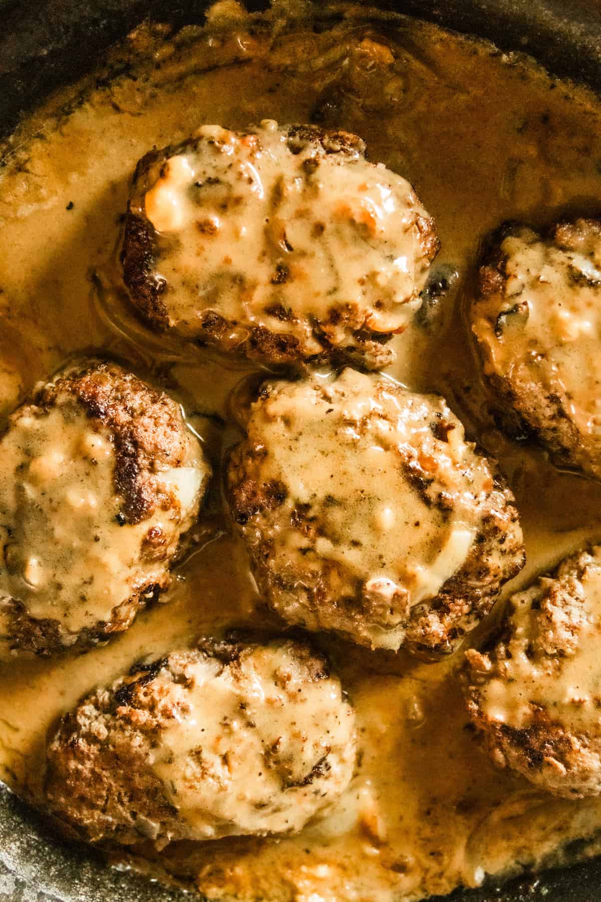 Venison salisbury steaks cooking in a cast iron skillet.