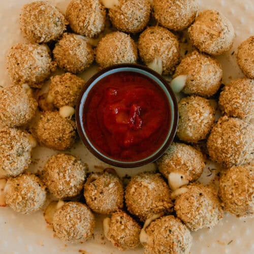 Whole wheat mozzarella cheese balls on a white serving plate with marinara sauce in a bowl in the middle.