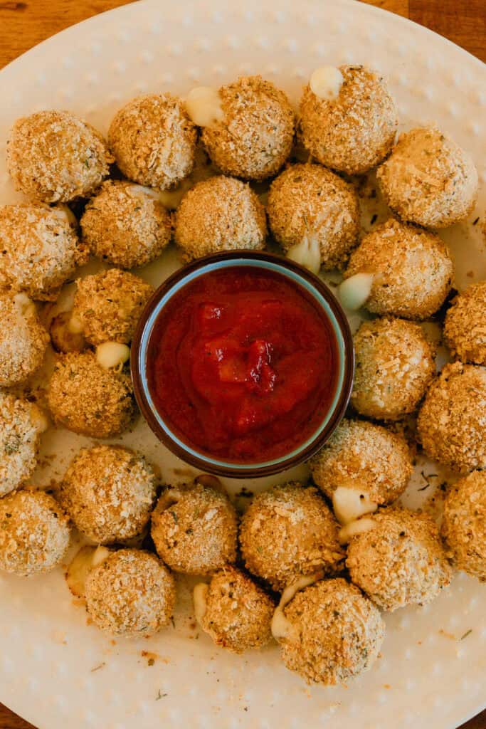Whole wheat mozzarella cheese balls on a plate with a bowl of marinara sauce.