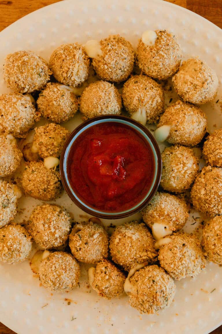 Whole wheat mozzarella cheese balls on a plate with a bowl of marinara sauce.