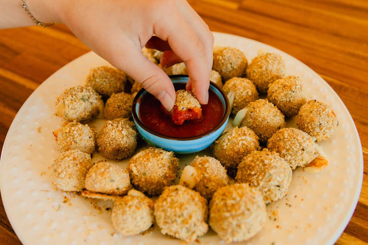 Dipping a cheese ball into a bowl of marinara sauce.