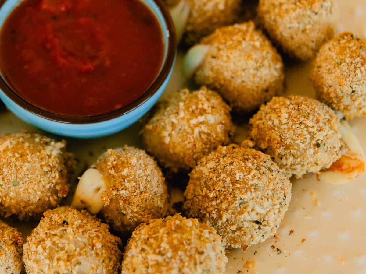 A close-up image of some whole wheat cheese balls on a plate next to a bowl of marinara sauce.