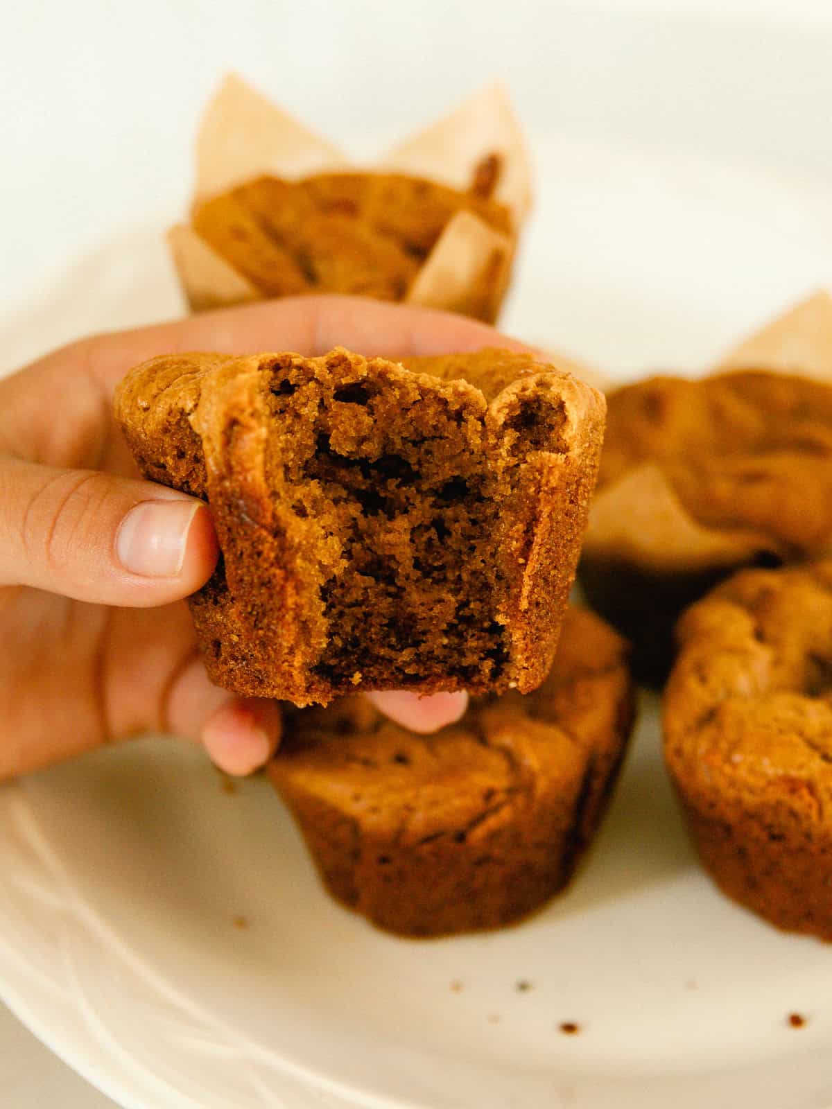 Holding up a peanut butter muffin with a bite take out and a plate of muffins in the background.