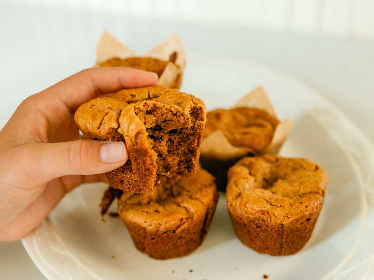 Holding a peanut butter muffin up over a plate of muffins.