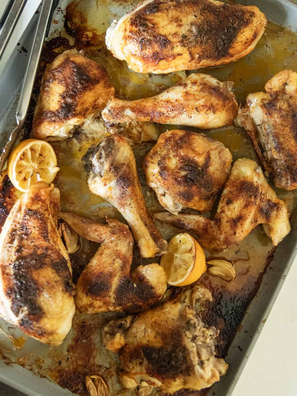 Roasted chicken quarters on a sheet pan with lemon halves.