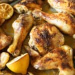 Roasted chicken quarters on a sheet pan with lemon halves.