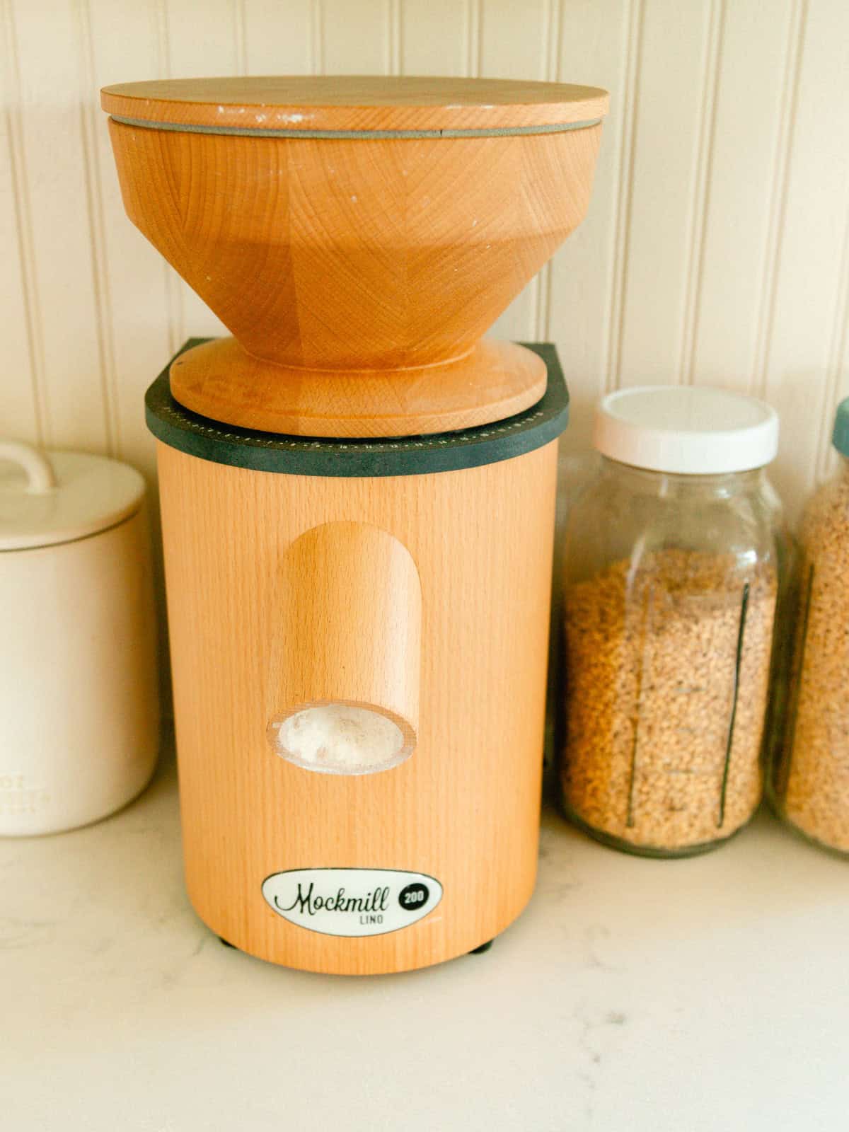 A grain mill with jars of whole wheat berries next to it.
