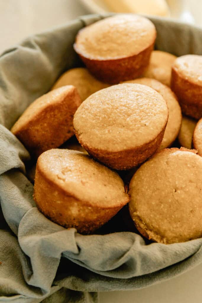 A basket of sweet corn muffins with a blue towel.