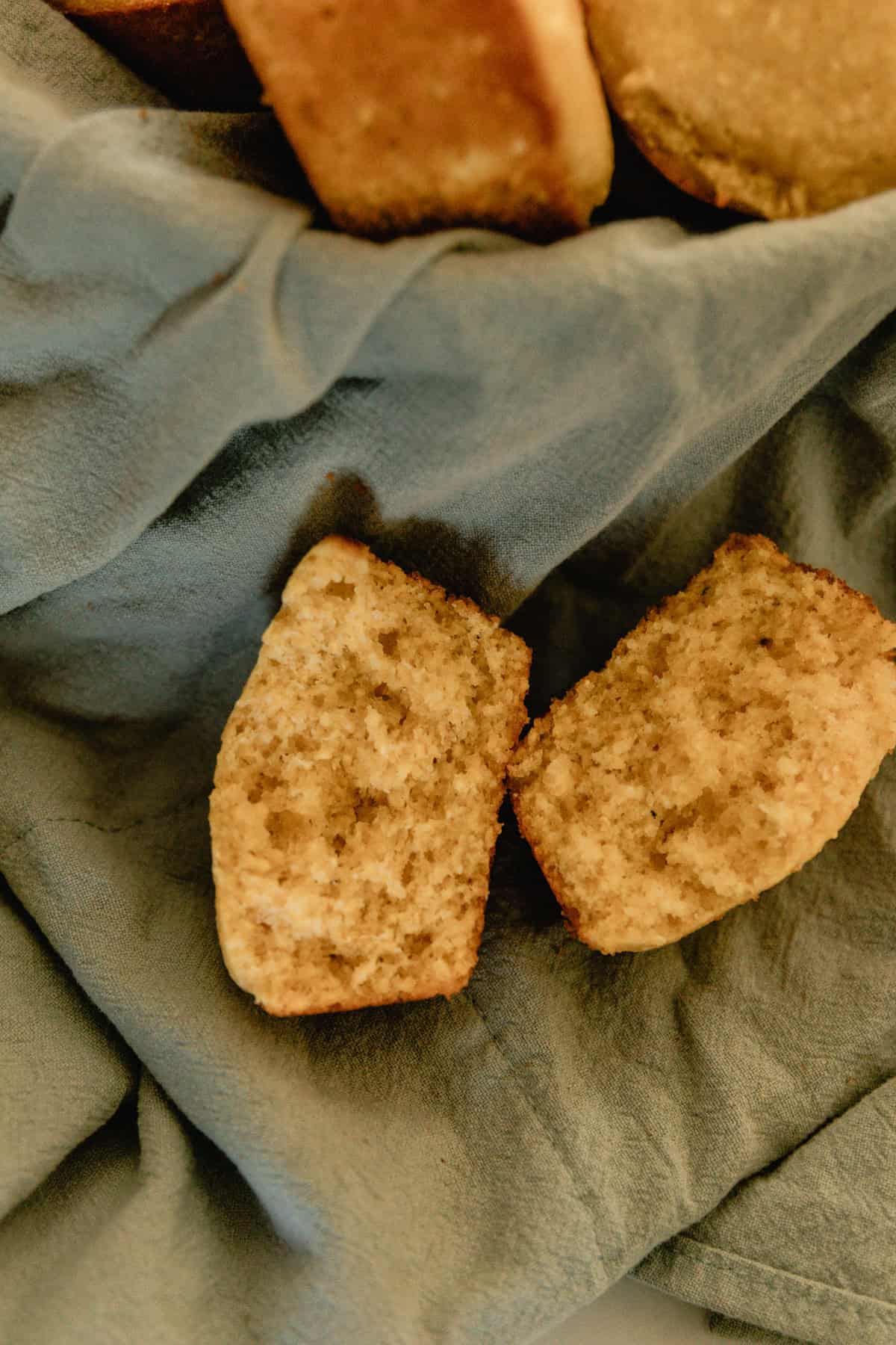 A sweet corn muffin split in half next to a basket of more muffins.