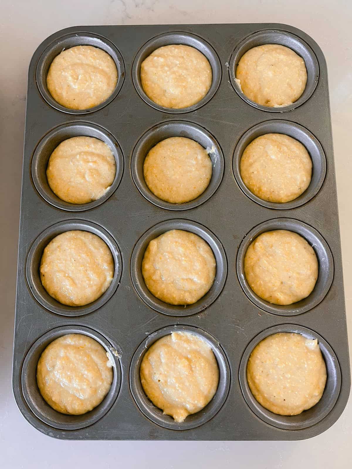 A muffin tin filled with sweet corn muffin batter.
