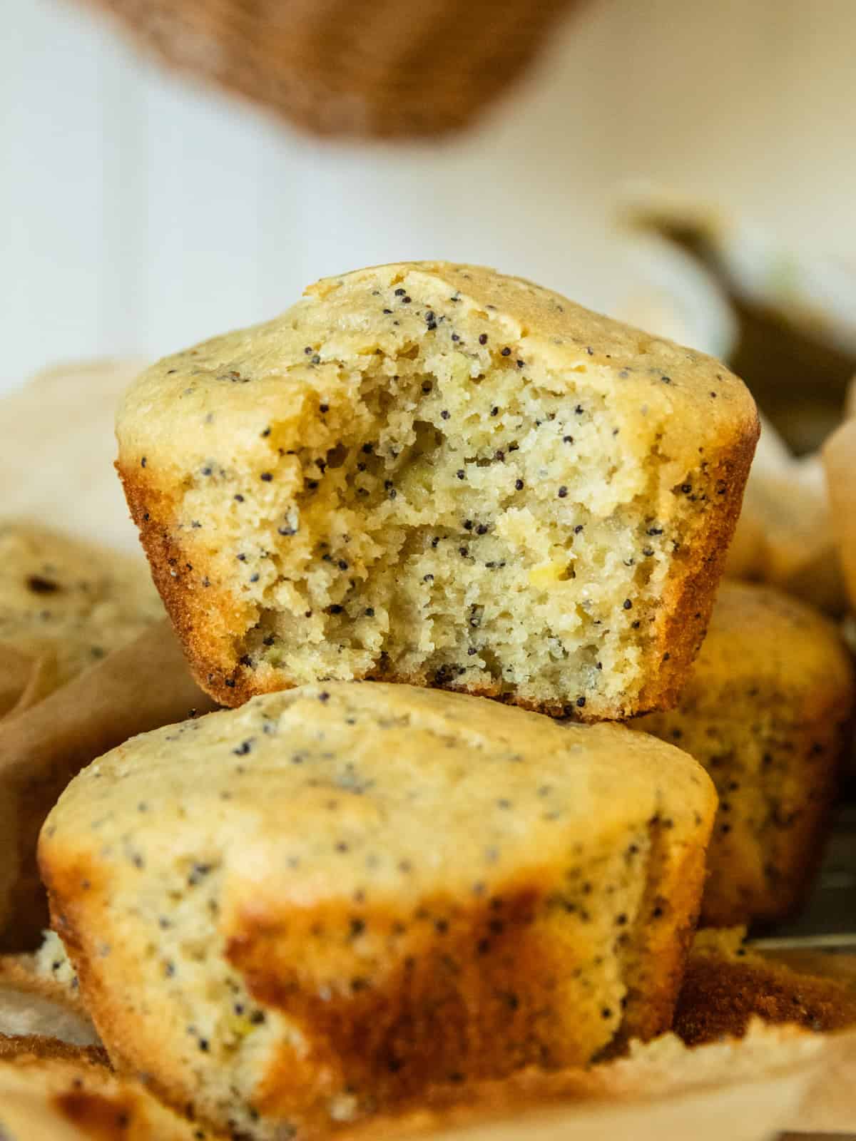 A lemon poppyseed muffin with a bite taken out of it, stacked on more muffins.