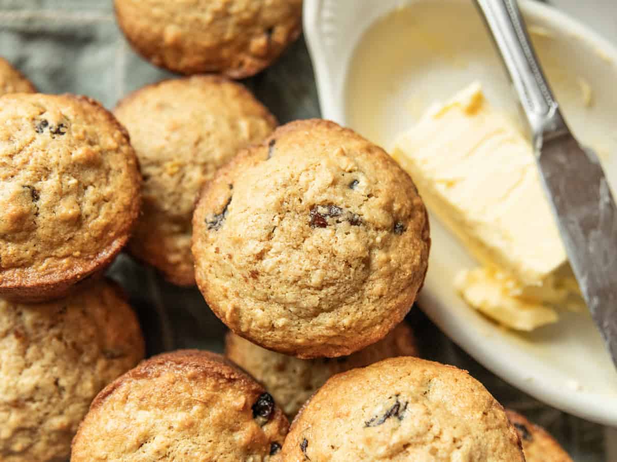 A pile of whole wheat oatmeal raisin muffins with butter on the side.