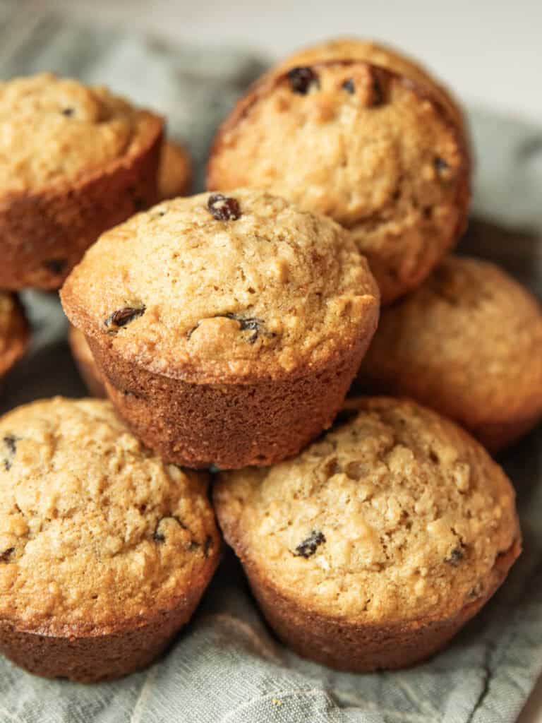 Whole wheat oatmeal raisin muffins stacked into a pile on a blue towel.