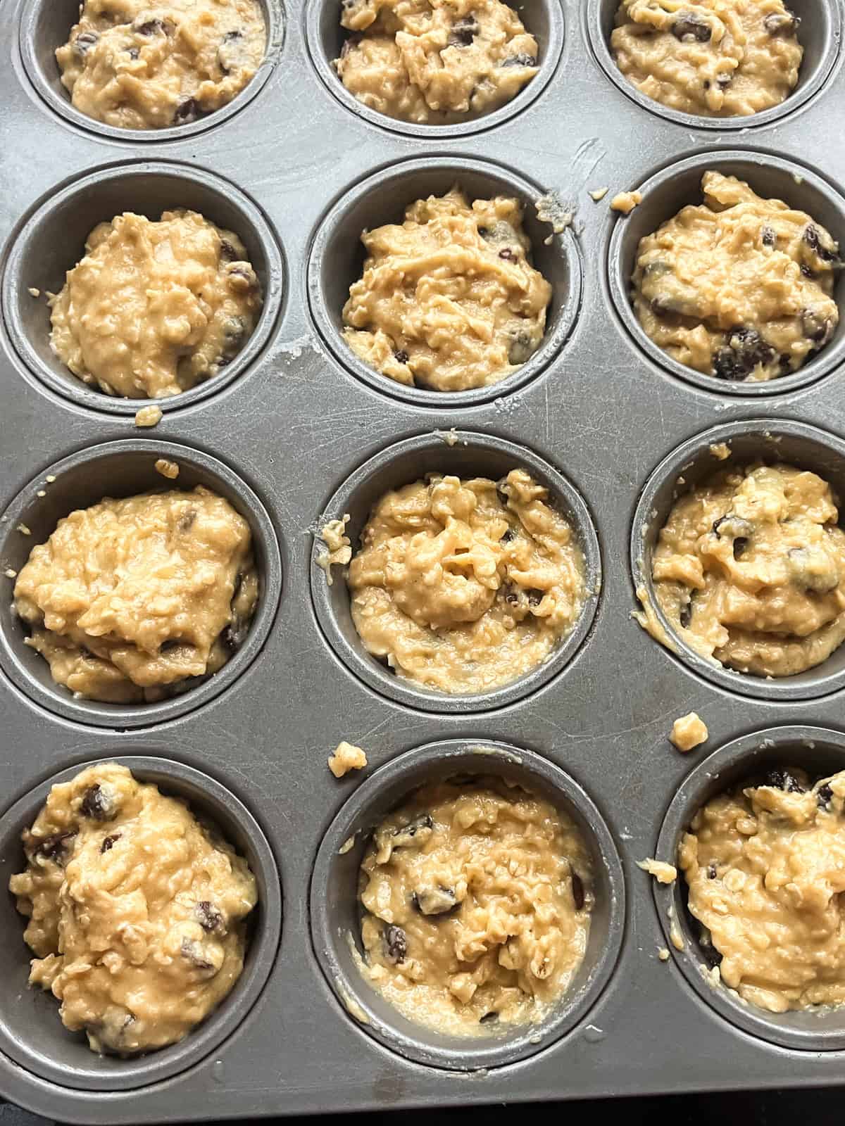 Oatmeal raisin muffin batter in a muffin tin.