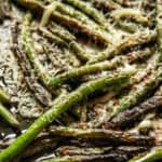 Cooked green beans in a cast iron skillet with parmesan cheese sprnikled on top.