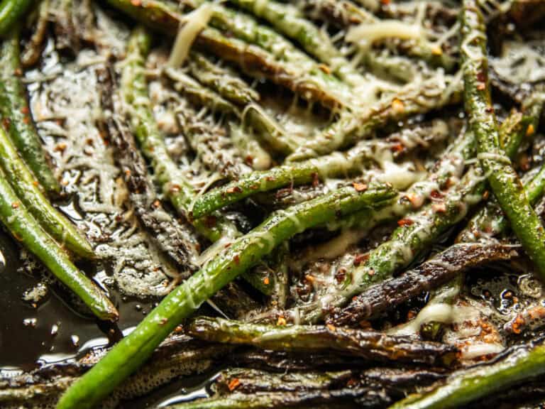 Cooked green beans in a cast iron skillet with parmesan cheese sprnikled on top.