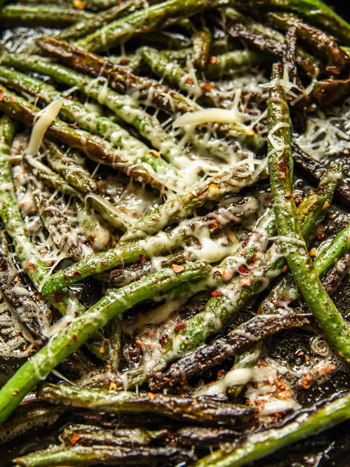 Cooked green beans in a cast iron skillet with parmesan cheese sprnikled on top.