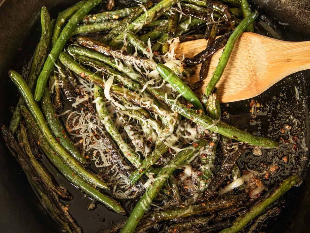 Scooping cast iron green beans with a wooden spoon.