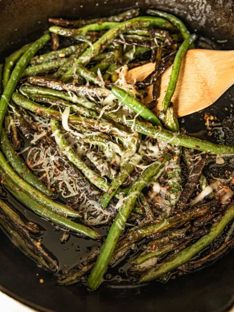 Cooked green beans sprinkled with cheese in a cast iron skillet.