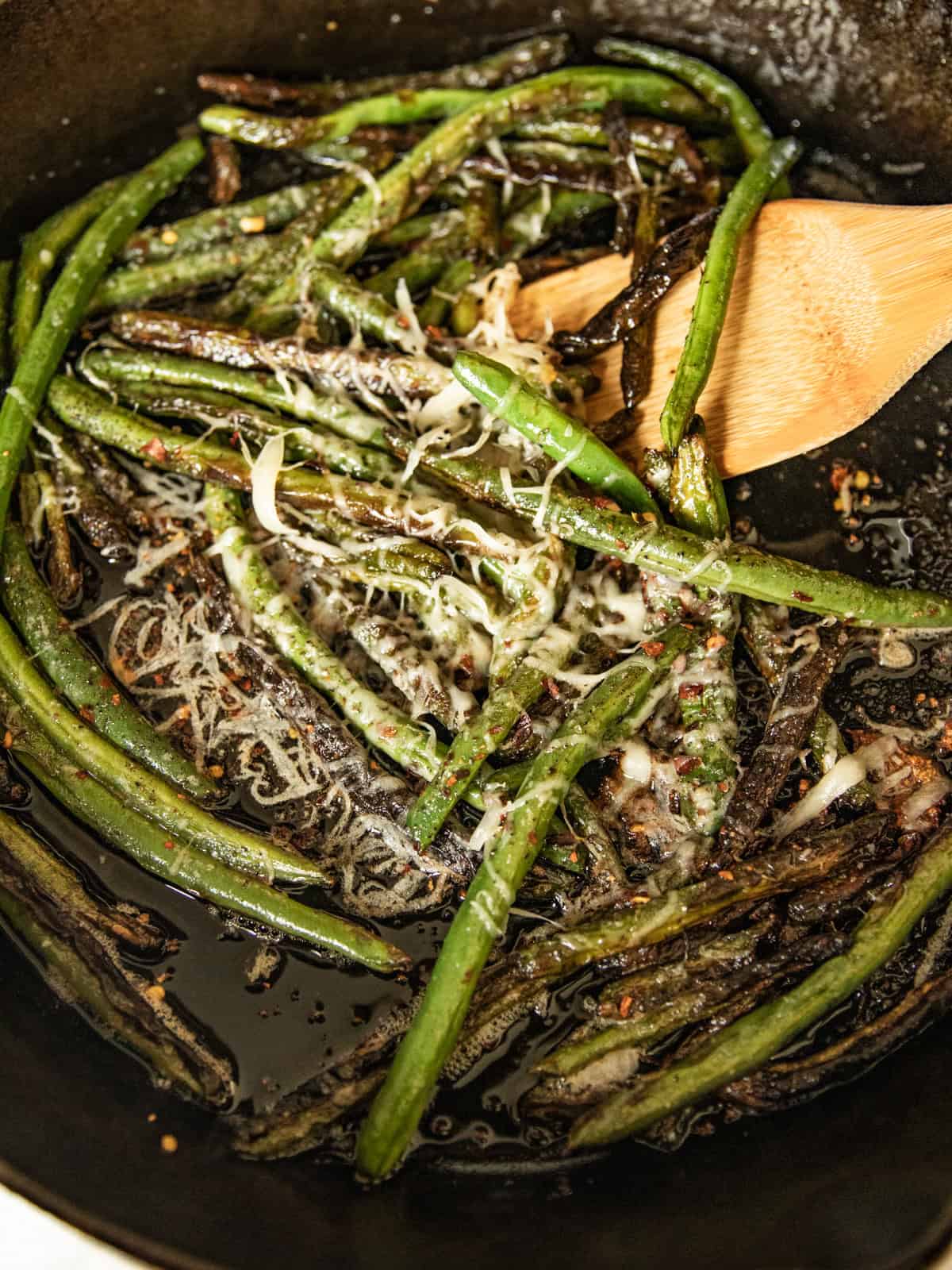 Cooked green beans sprinkled with cheese in a cast iron skillet.