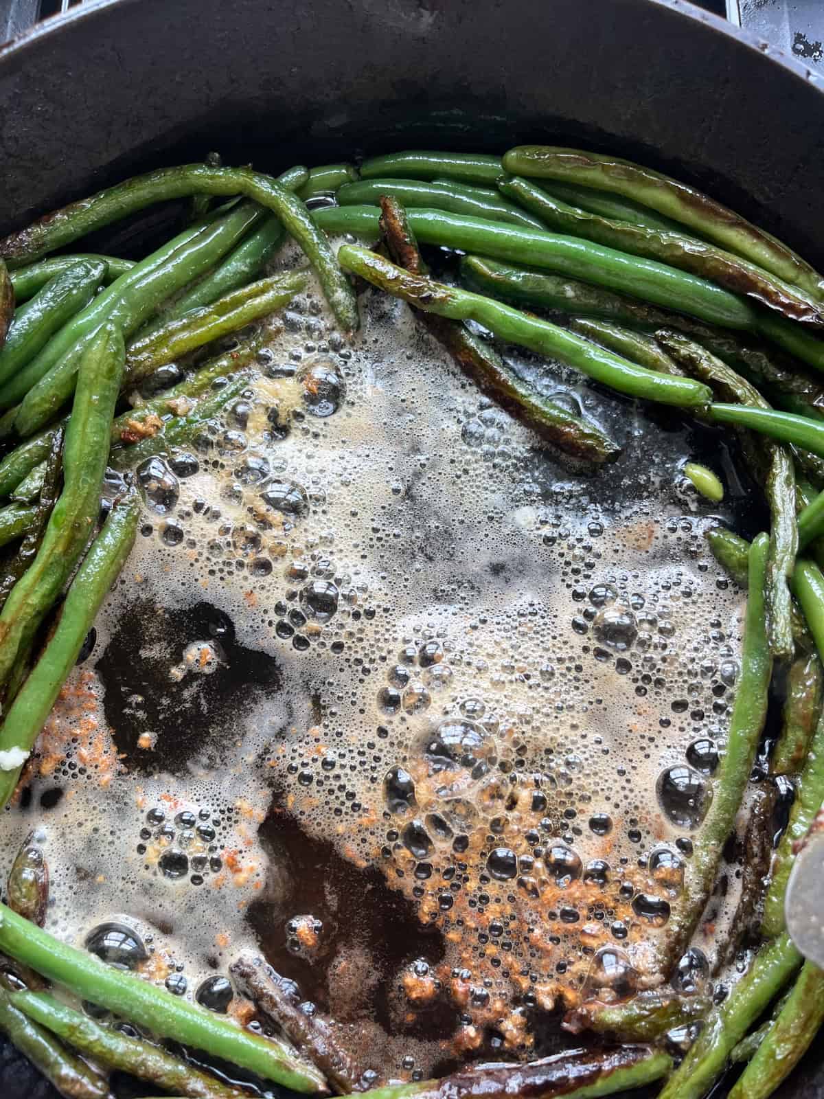 Cooked green beans pushed to the side of the pan with butter melting in the center.