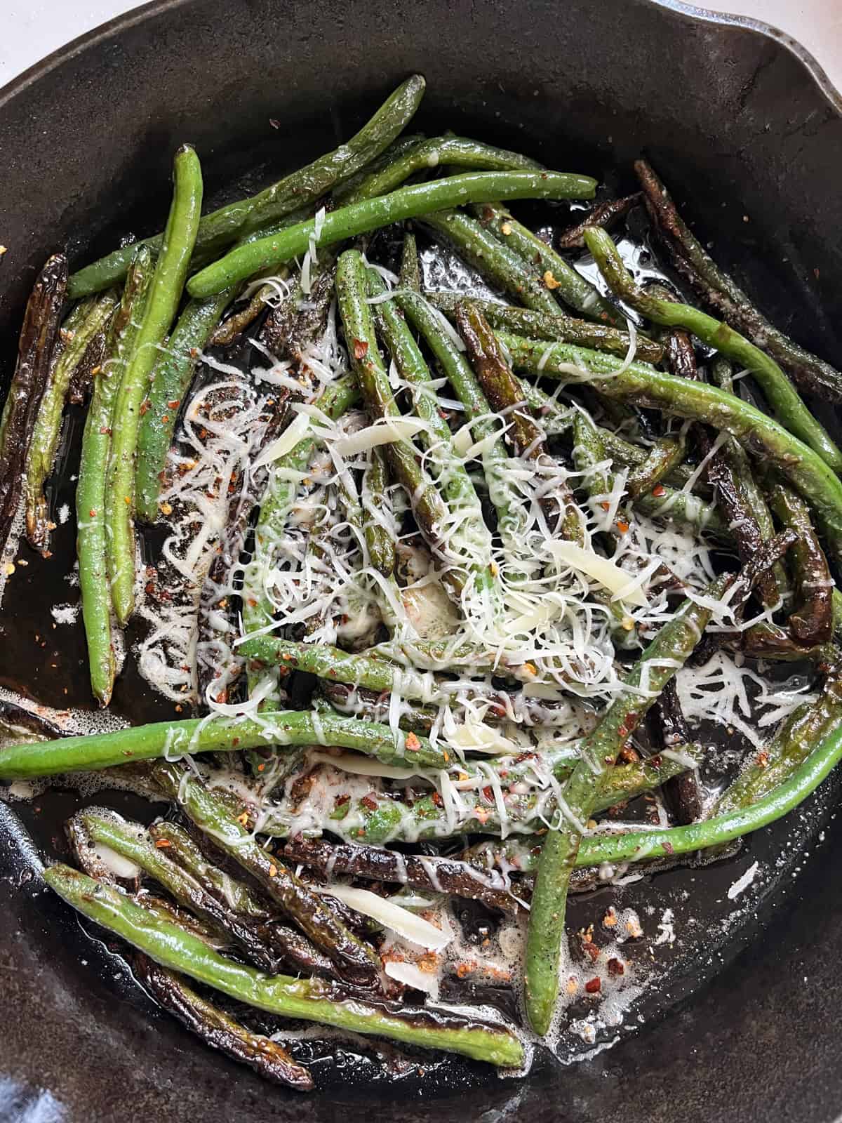 Cooked green beans in a cast iron skillet with parmesan cheese on top.