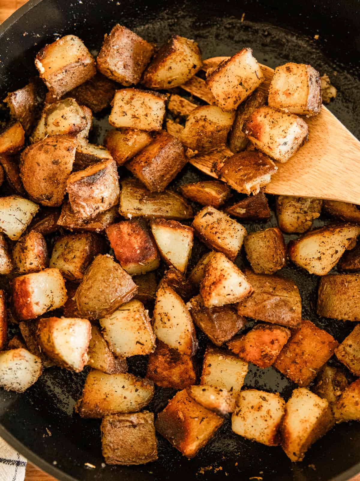 Scooping cast iron skillet potatoes out of a skillet with a wooden spoon.