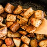 Scooping cast iron skillet potatoes out of a skillet with a wooden spoon.