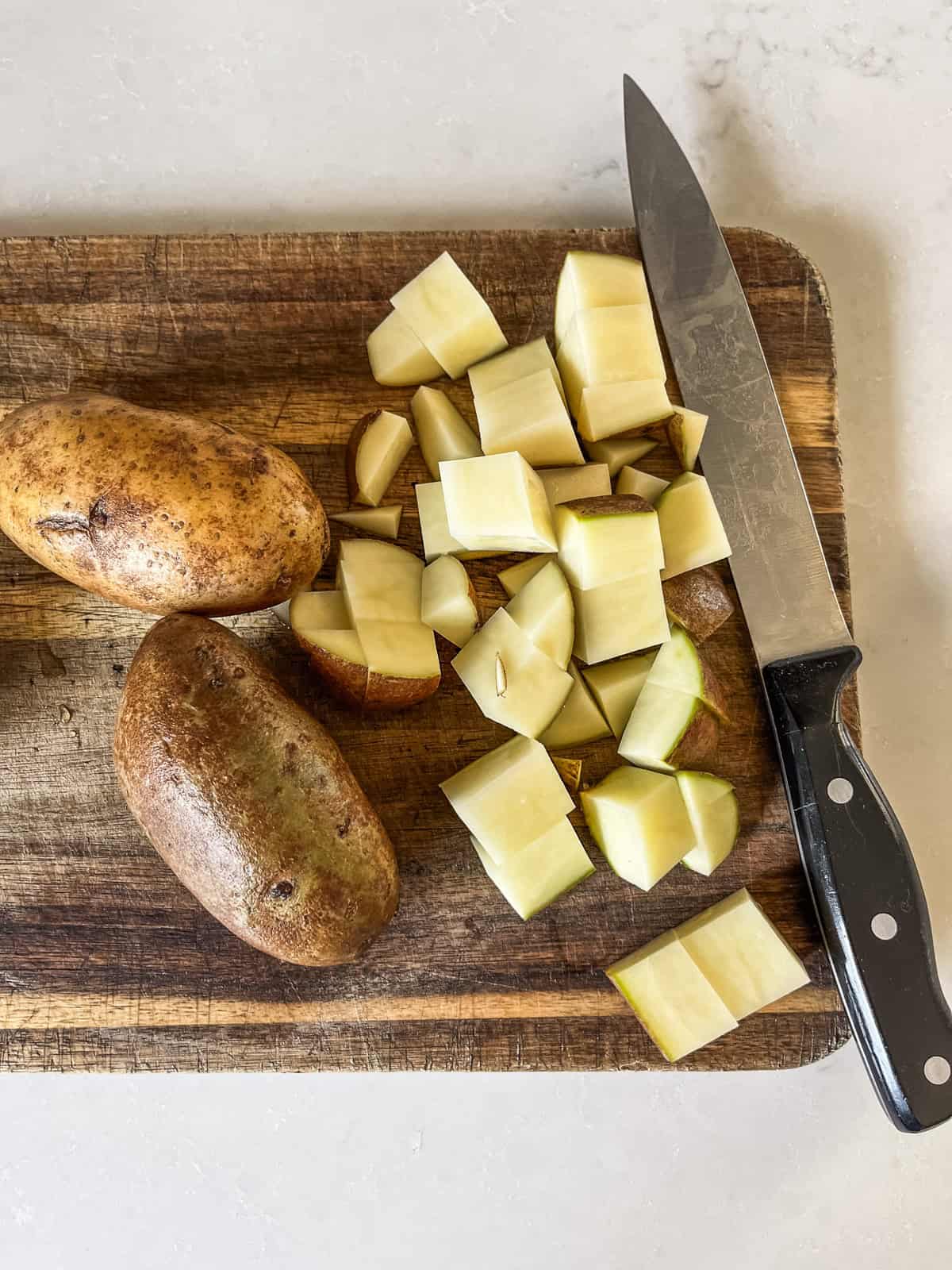 Cubing russet potatoes on a wooden cutting board.
