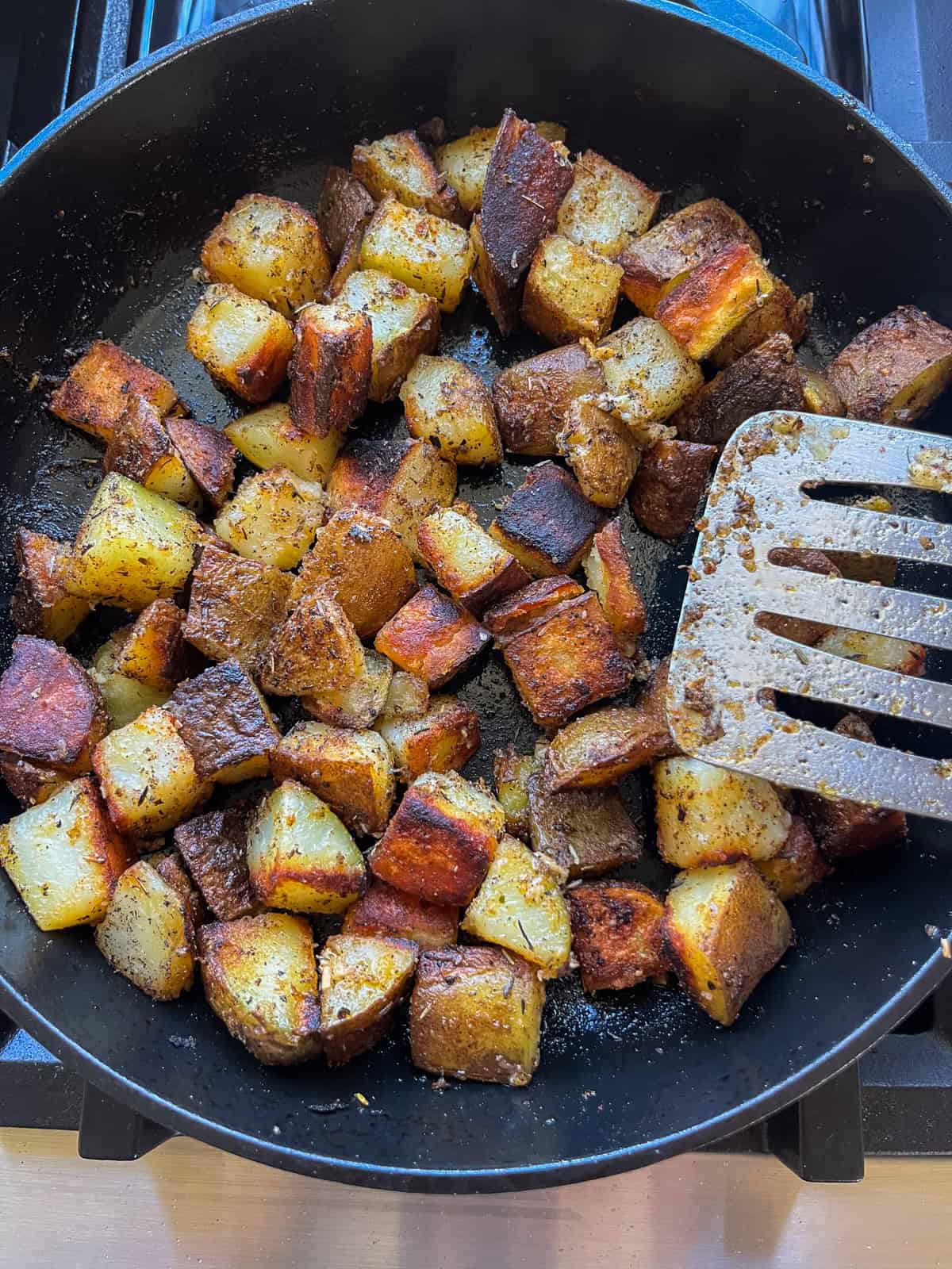 Crispy fried cast iron skillet potatoes in a skillet with a spatula stirring them.