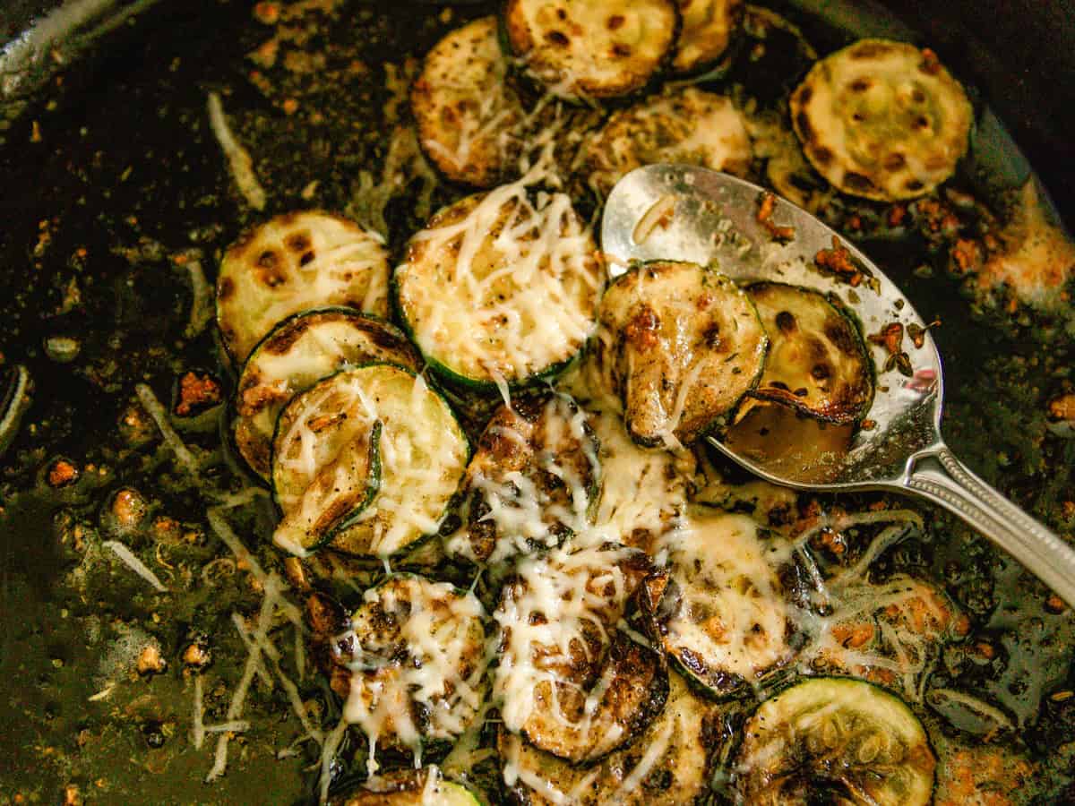 Scooping zucchini rounds out of a cast iron skillet.