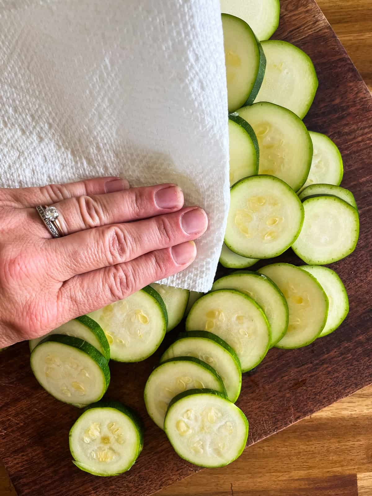 Patting dry sliced zucchini rounds with a paper towel.