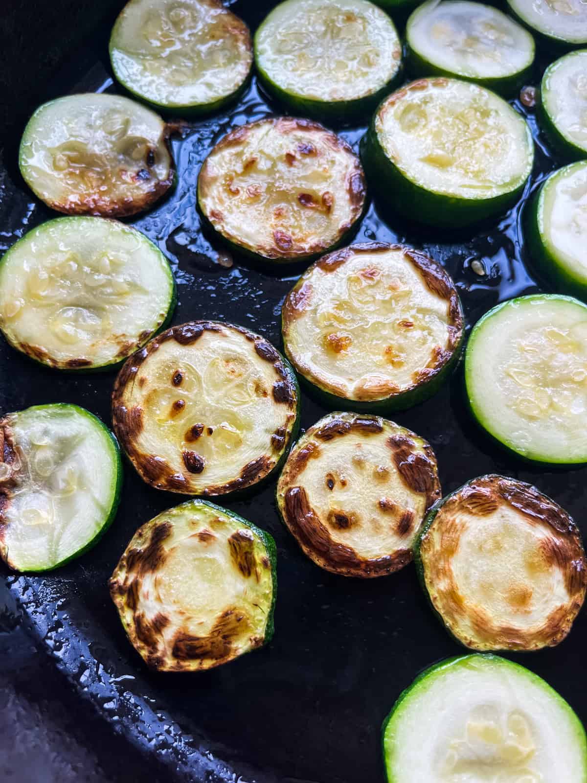 Golden brown zucchini in a cast iron skillet after the initial flip.