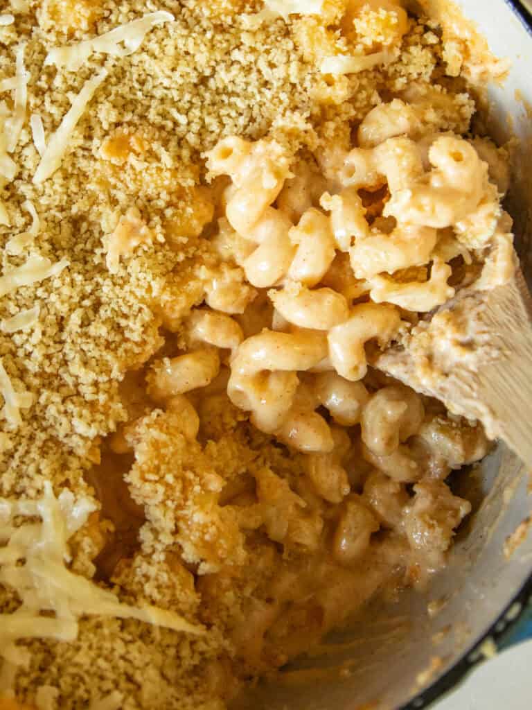 Scooping dutch oven mac and cheese with a wooden spoon.