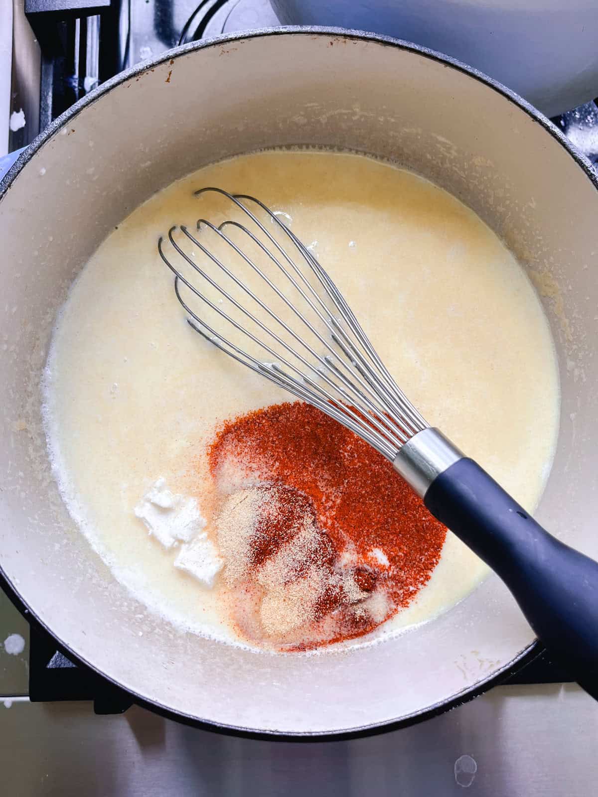 Cream cheese and spices added to a dutch oven with milk mixture.