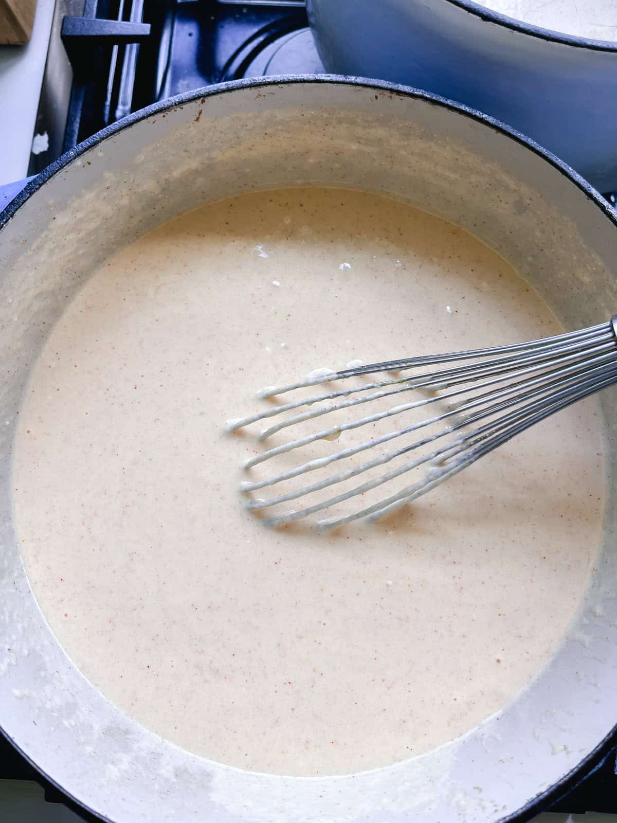 Stirring milk mixture in a dutch oven with a whisk.
