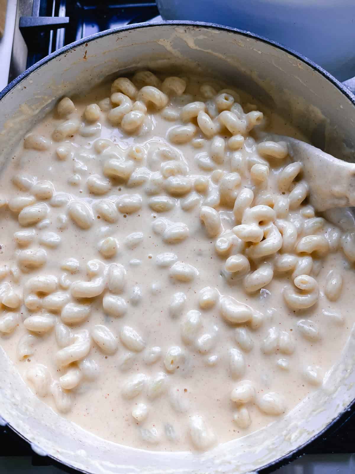 Stirring cooked noodles into cheese mixture for dutch oven mac and cheese.