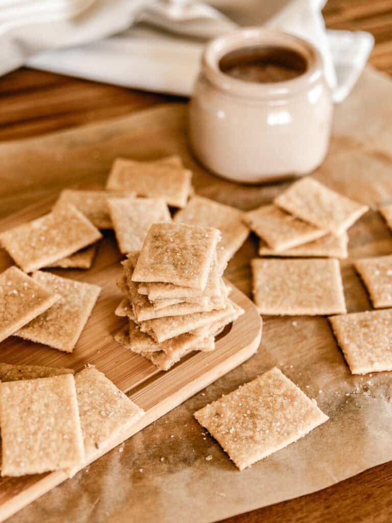 Fresh milled flour crackers scattered on a piece of parchment paper with a salt well in the background.