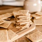 A stack of fresh milled flour crackers surrounded by more crackers on a wooden cutting board.