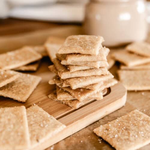 A stack of fresh milled flour crackers surrounded by more crackers on a wooden cutting board.