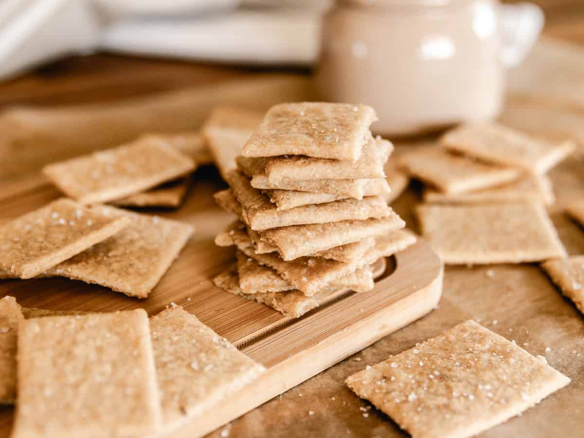 A stack of fresh milled flour crackers surrounded by more crackers on a wooden cutting board.