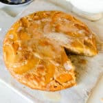 A peach upside down cake with a slice taken out of it, on a white serving board.