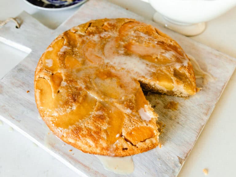 A peach upside down cake with a slice taken out of it, on a white serving board.