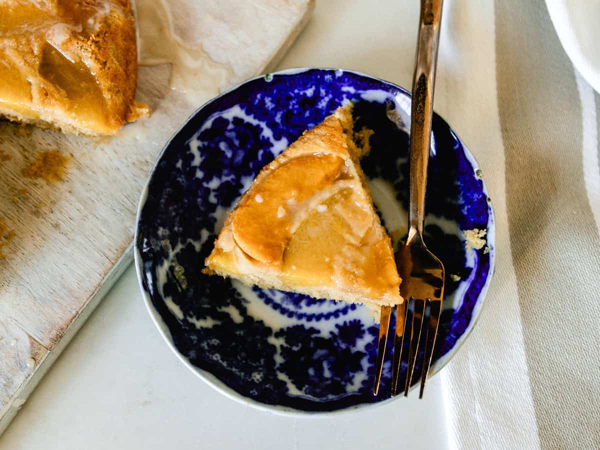 A slice of peach upside down cake on a blue plate with a fork.