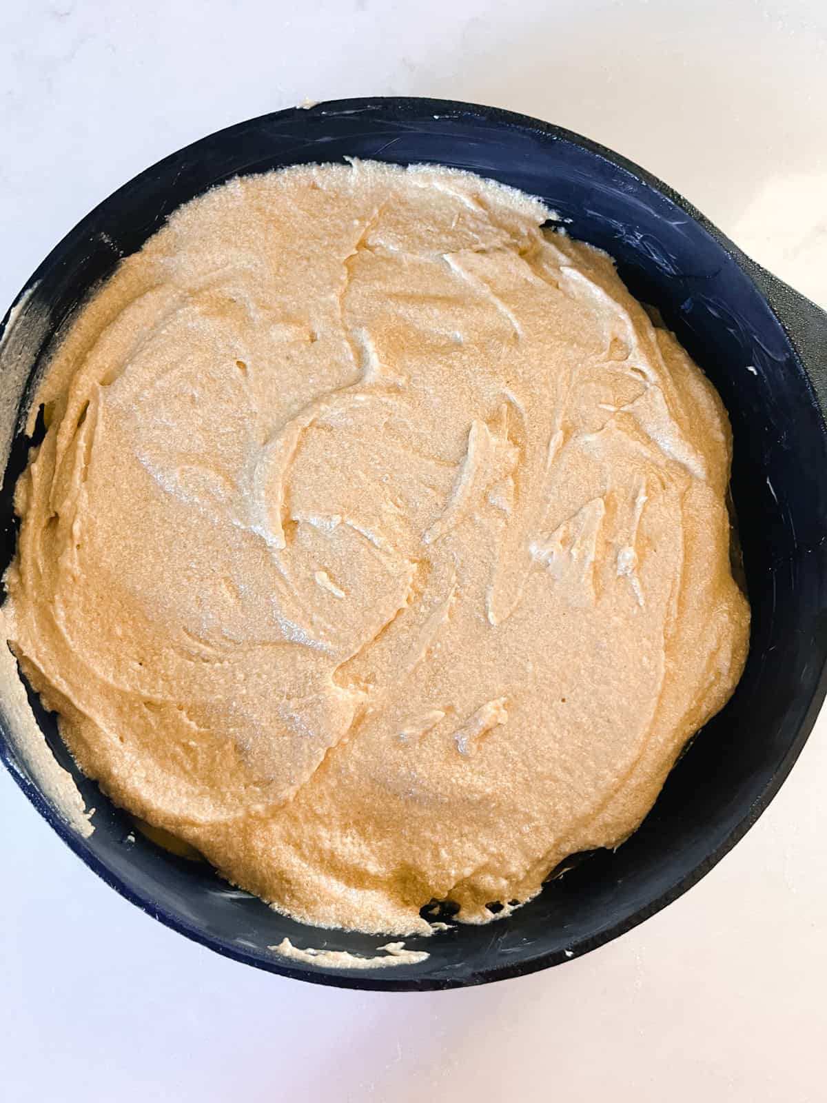 Peach upside down cake batter spread in a cast iron skillet.