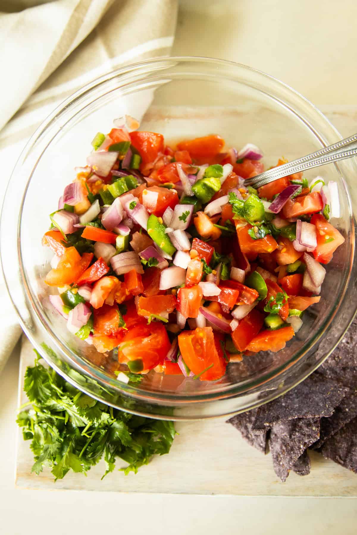 A bowl of pico de gallo on a towel with chips and cilantro.