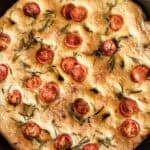 A close up of freshly milled focaccia bread in a cast iron skillet.
