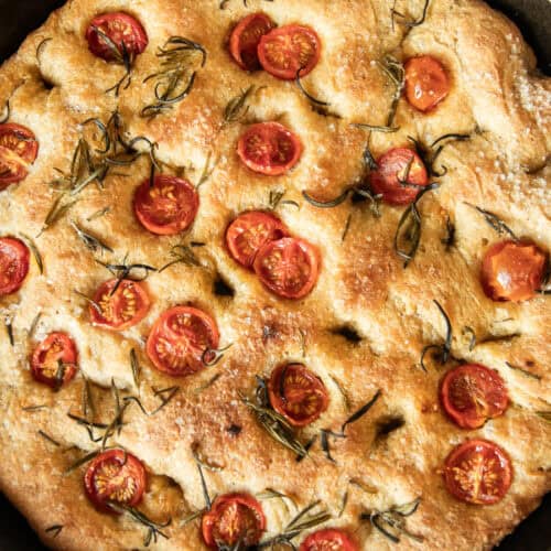 A close up of freshly milled focaccia bread in a cast iron skillet.